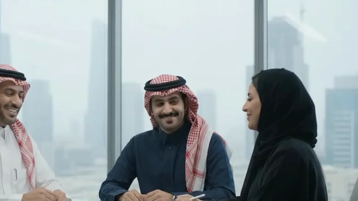 Two colleagues smiling as a third listens across a meeting table